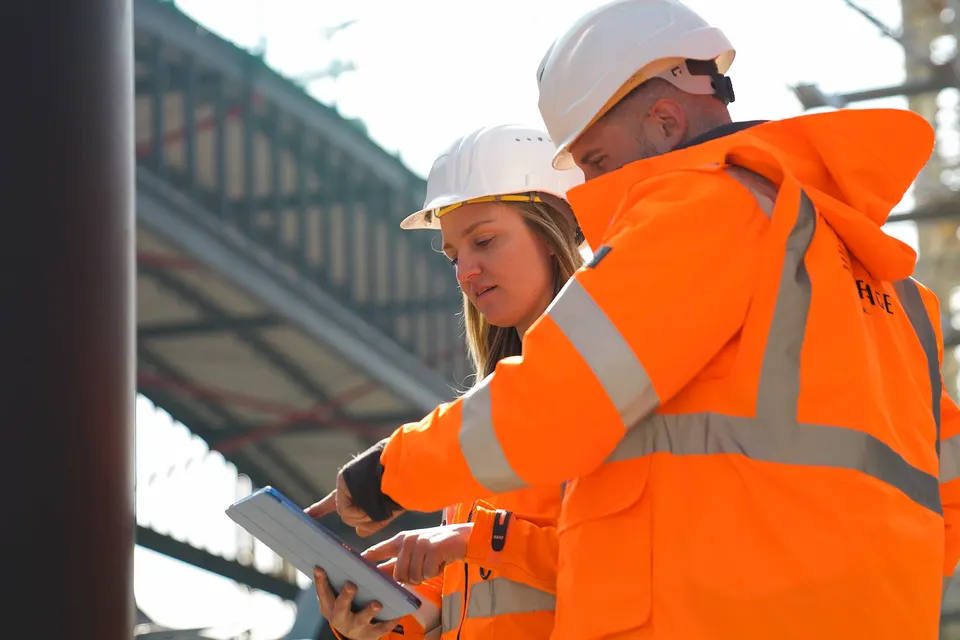Zwei Mitarbeitende mit Helm und Tablet auf einer Baustelle