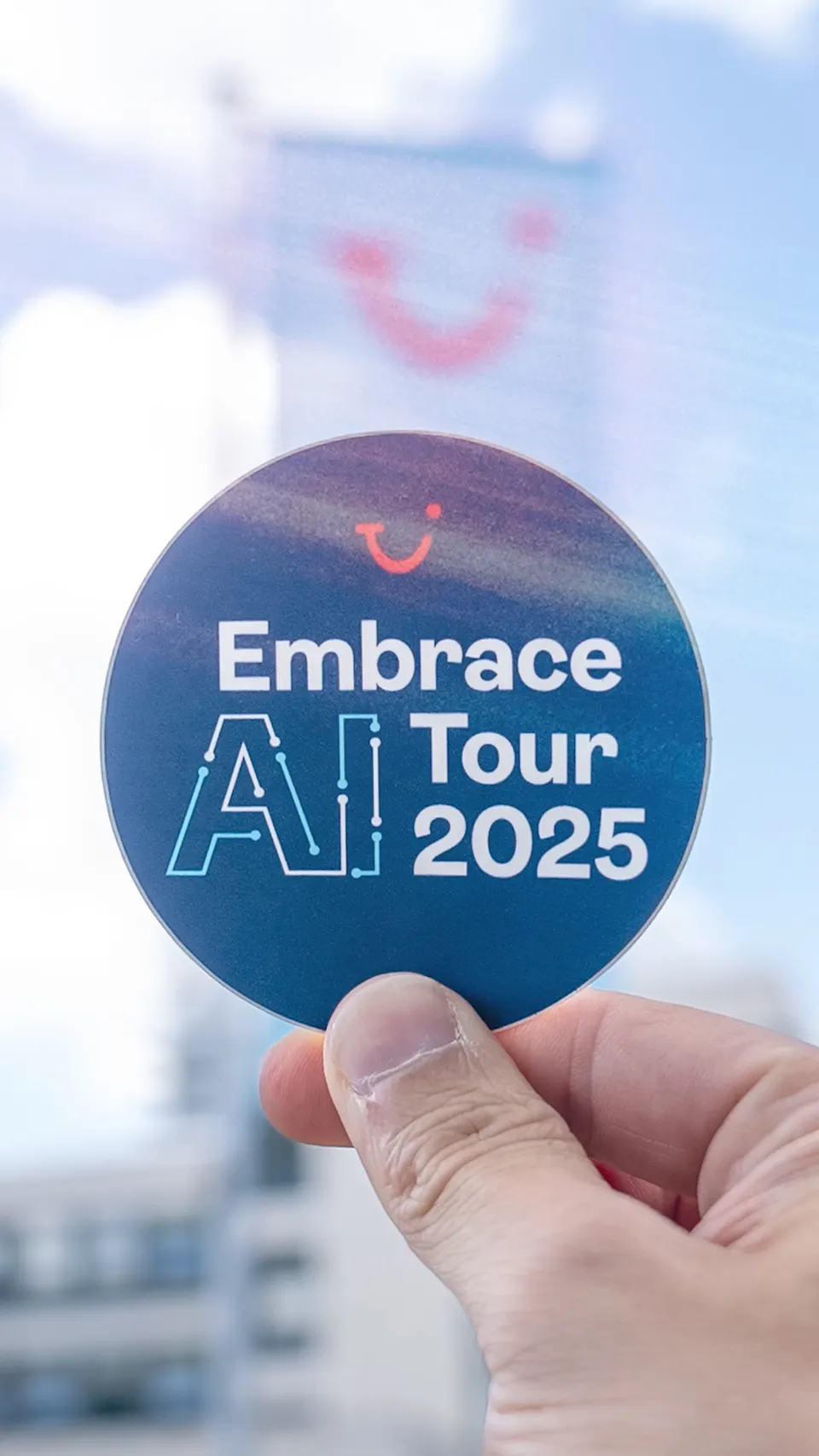 Hand hält einen Sticker der TUI Embrace AI Tour 2025
