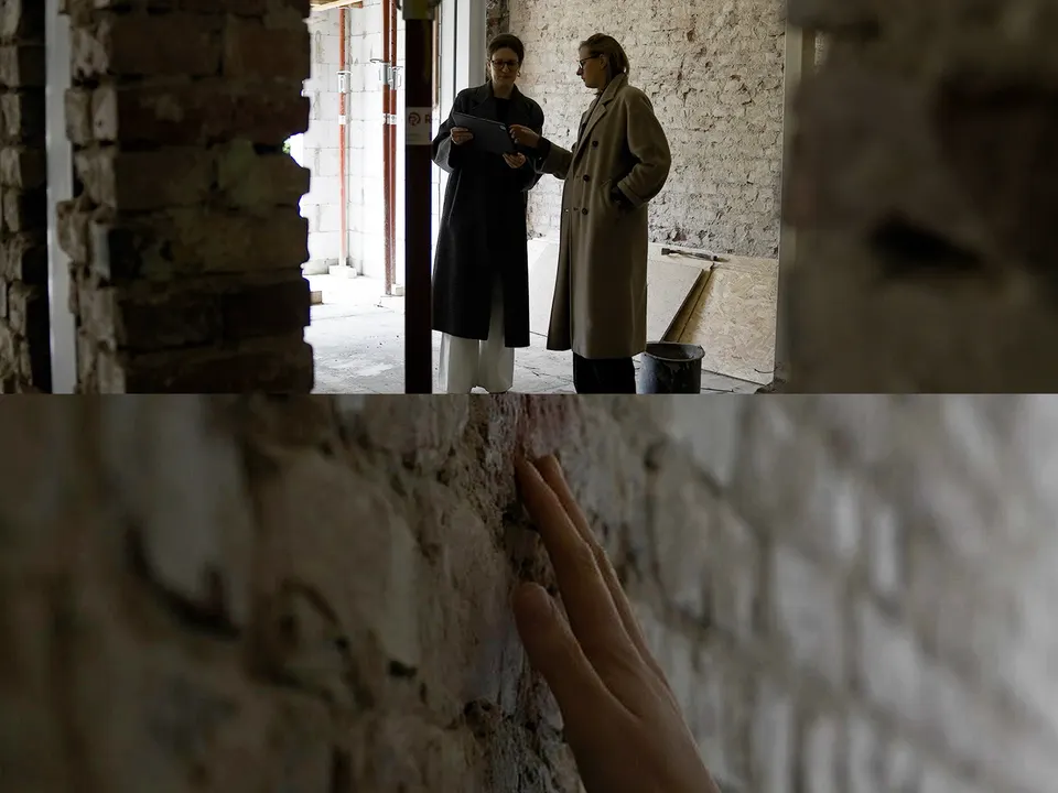 Zwei Architekten in einem Rohbau, Hand an einer Backsteinwand